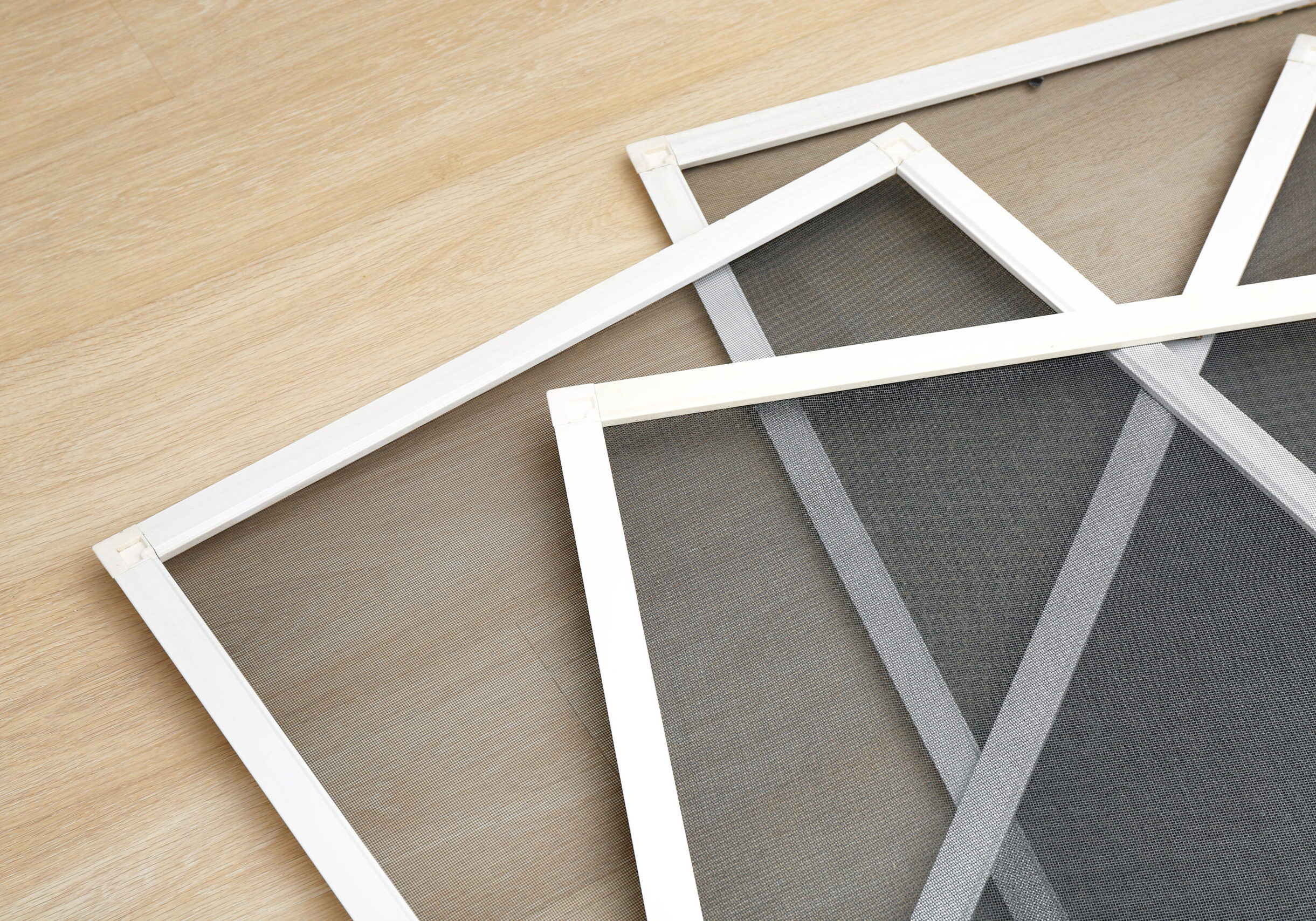 Three white framed window screens overlapping on a wood floor.