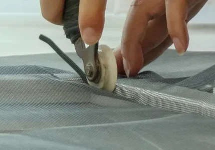 Close-up of hands pressing screen spline into frame using a roller tool