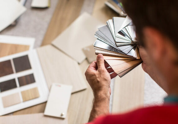 Person holding a fanned-out set of wood and metal finish samples over a table with additional sample swatches